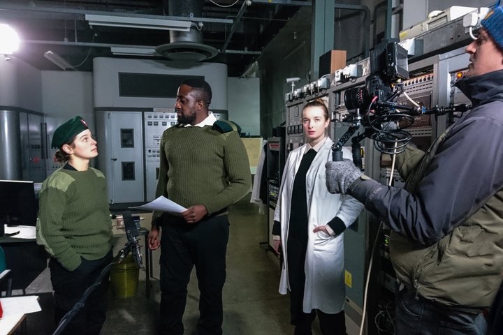 Behind the scenes at film set showing actors performing a scene to camera